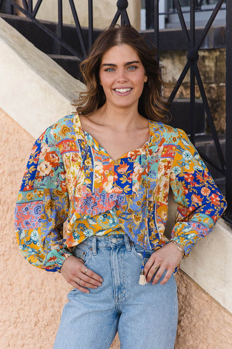 Woman wearing a colorful floral blouse and blue jeans standing outdoors.