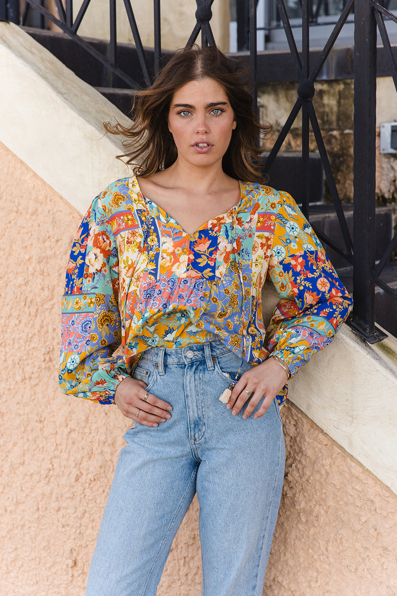Woman wearing a colorful floral blouse and blue jeans standing outdoors.